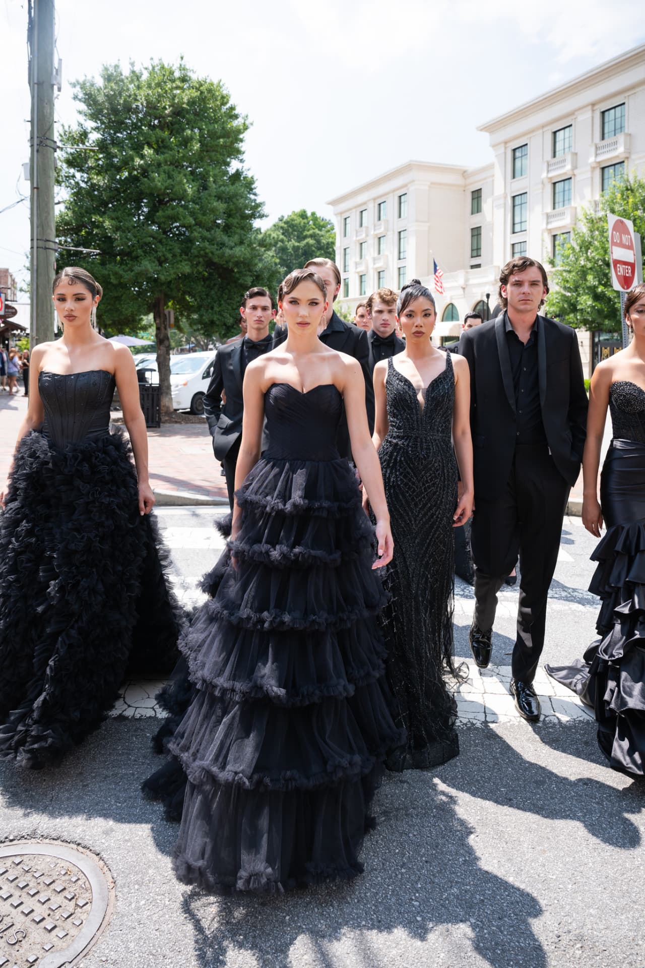 Model in a tiered black tulle gown leading the group across the street