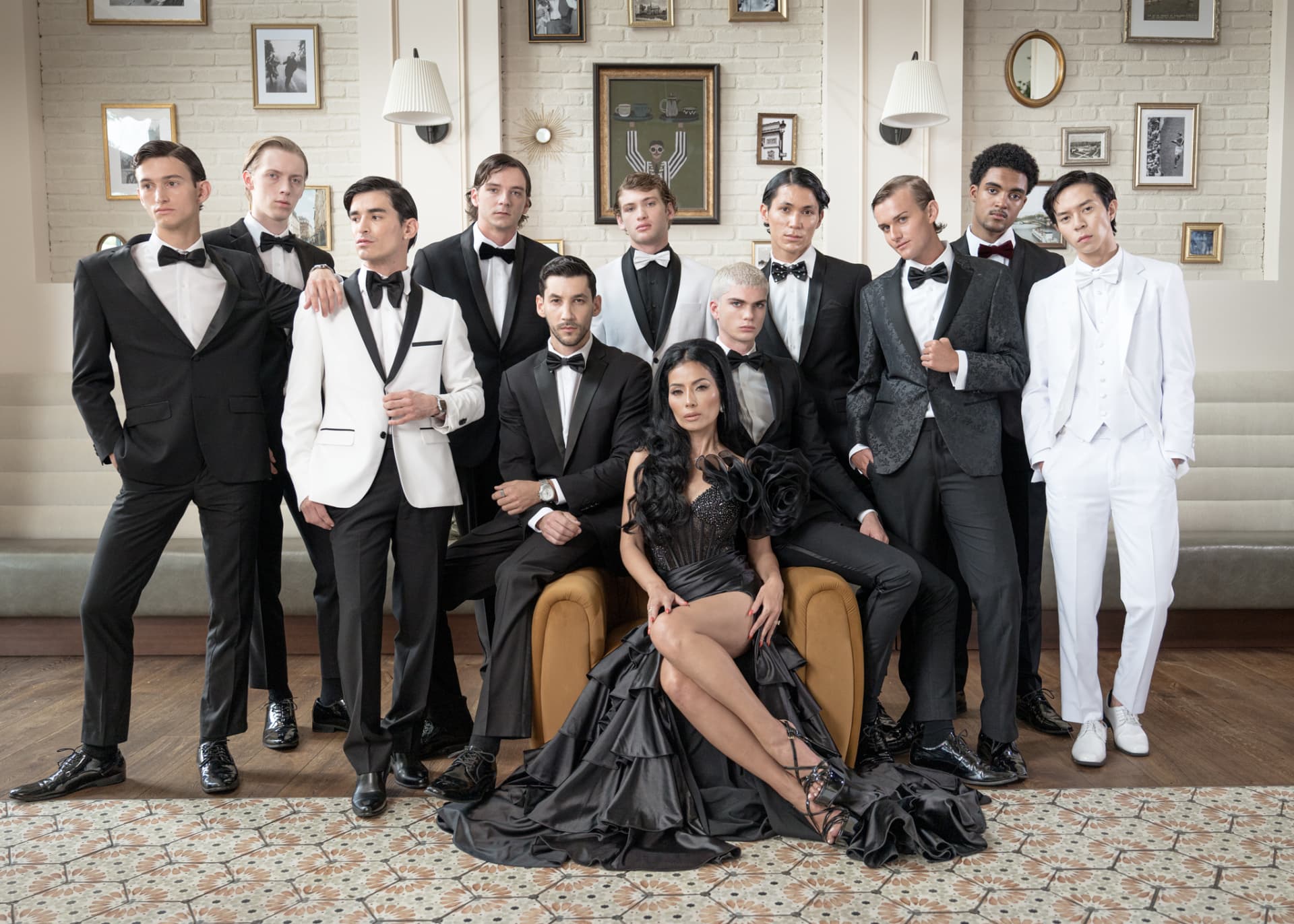 Menswear cast in tuxedos surrounding a seated model in black couture